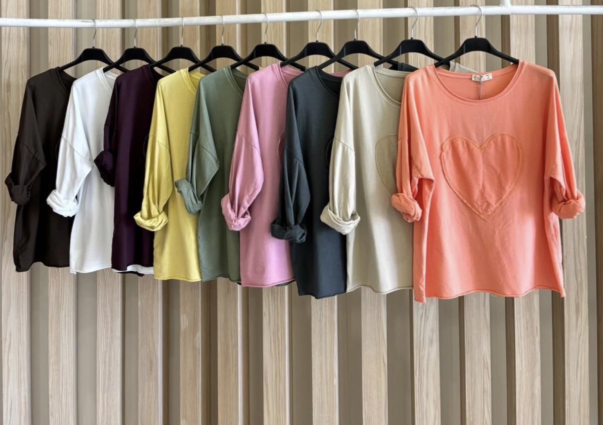 Dez camisolas de manga comprida em várias cores, com coração bordado no peito, penduradas num cabide branco