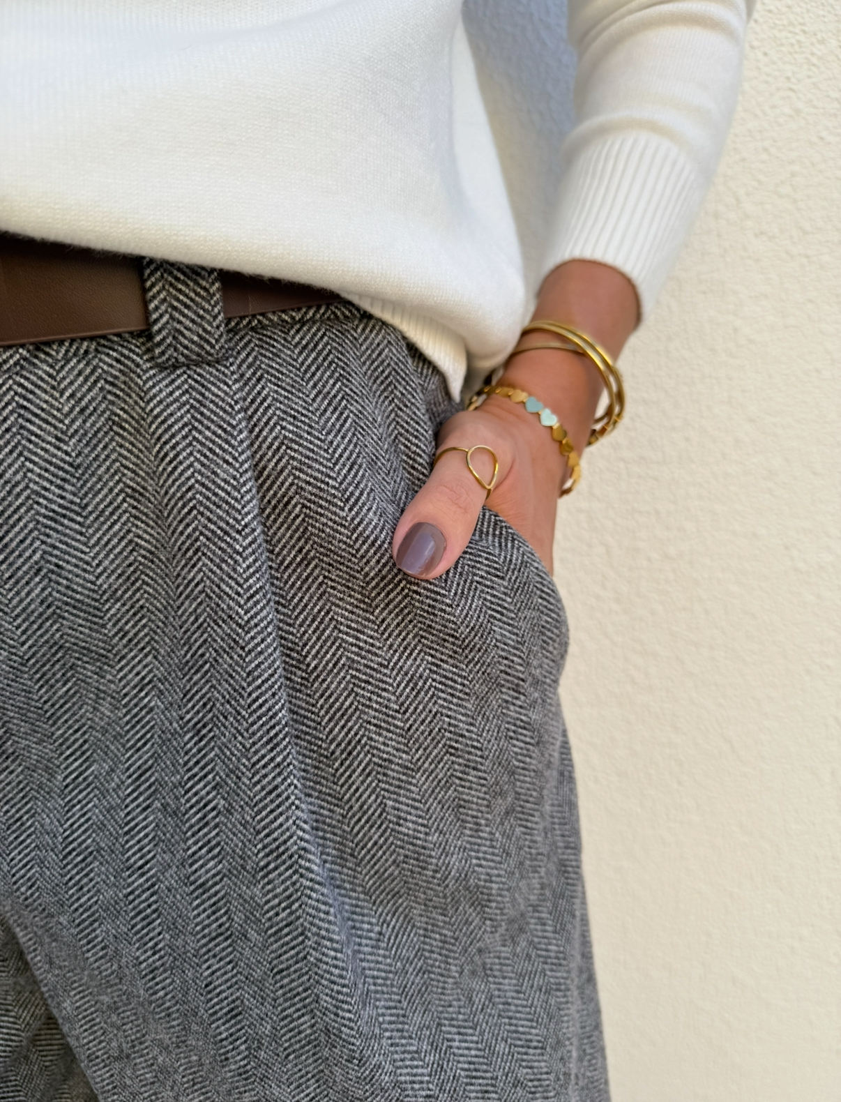 Camisola branca, calças em padrão espinha de peixe cinzentas e acessórios dourados