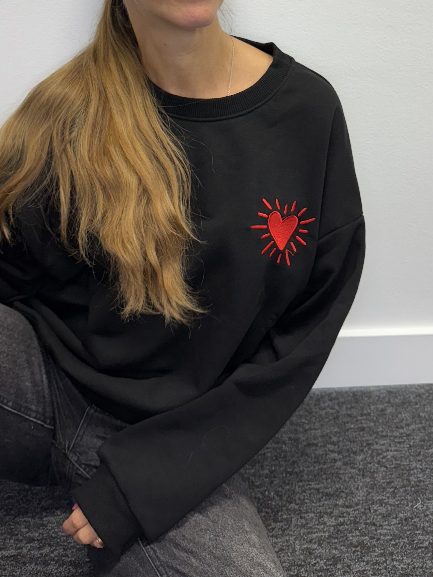 Pessoa a usar sweatshirt preta com coração vermelho bordado no peito.