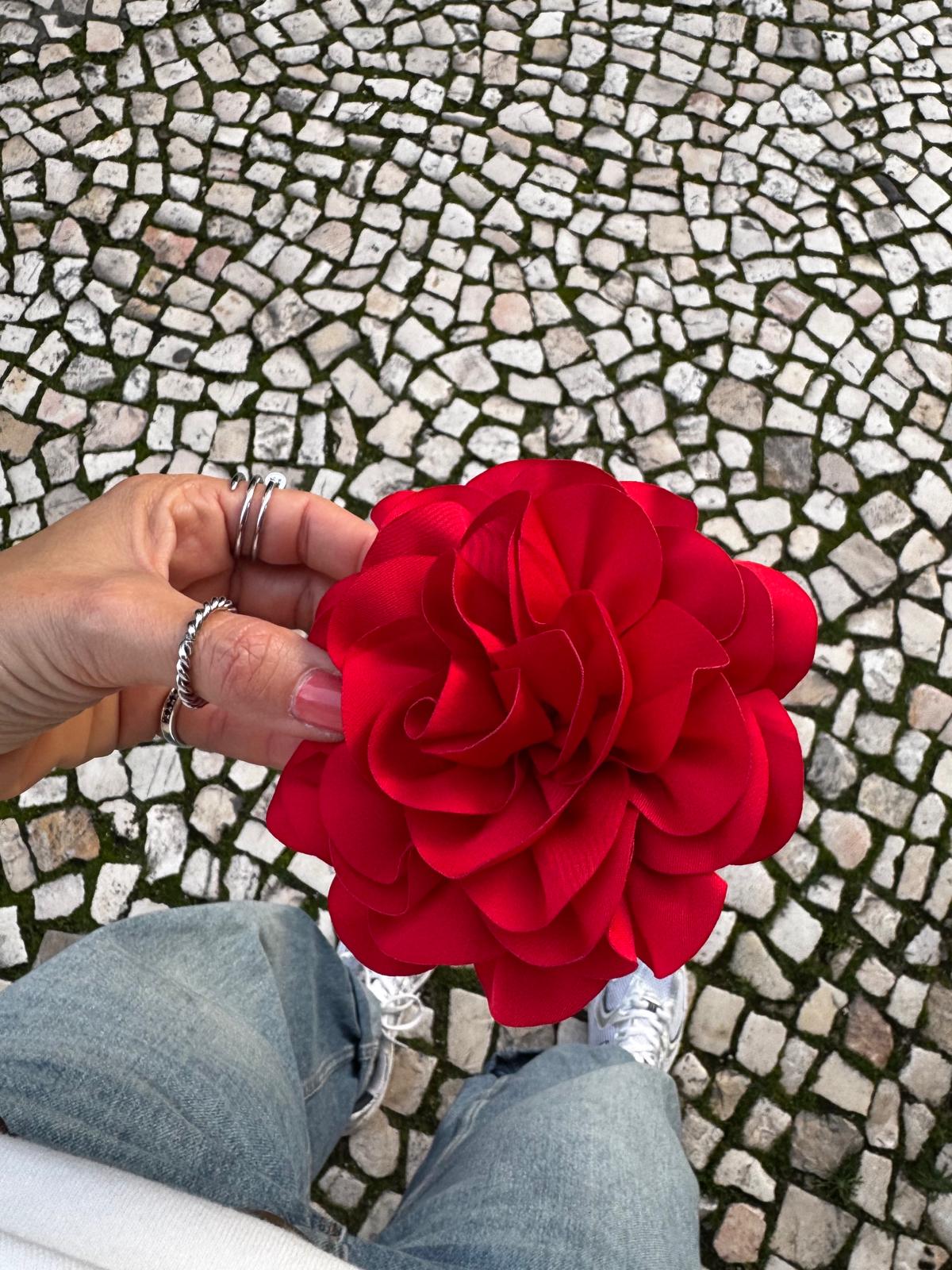 Mão segurando flor vermelha de tecido com calçada portuguesa ao fundo