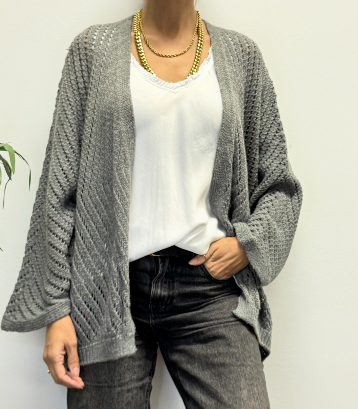 Casaco cinzento de malha grossa, camisola branca e calças pretas com colares dourados