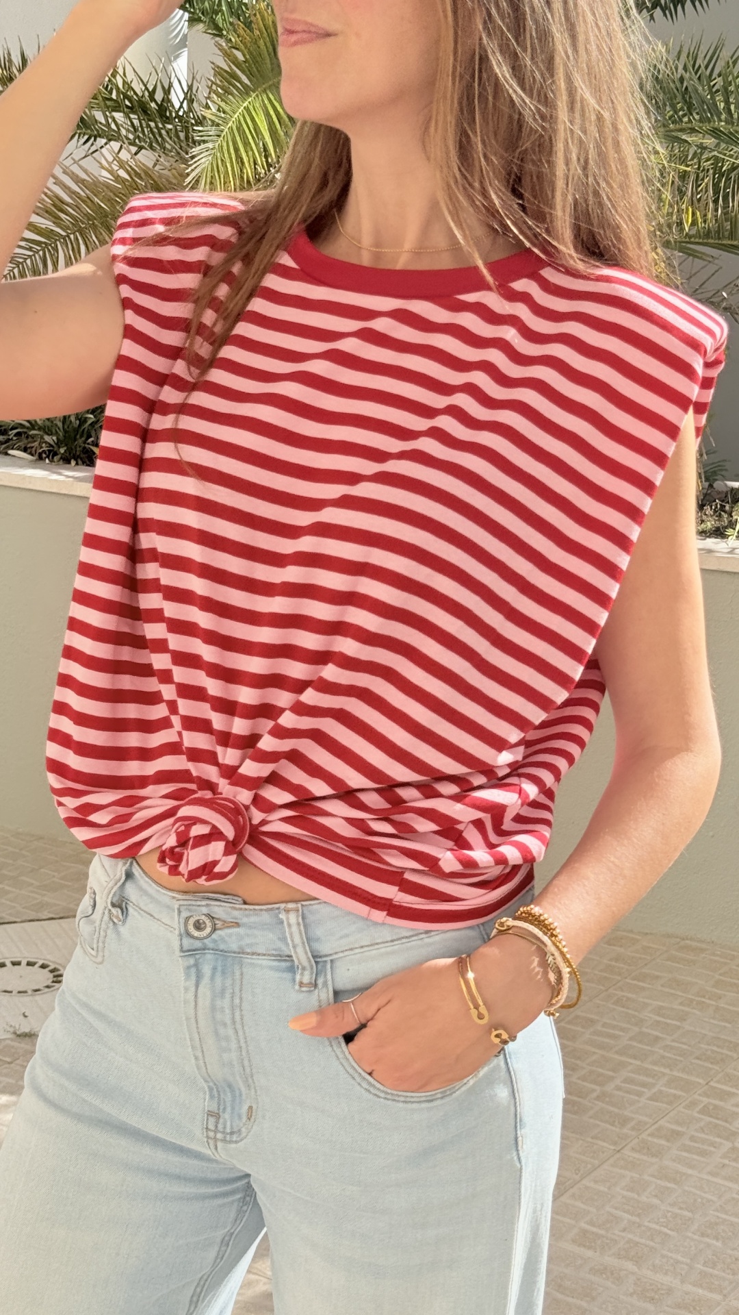 T-shirt às riscas vermelhas e claras com nó frontal, usada com jeans claros e pulseiras douradas