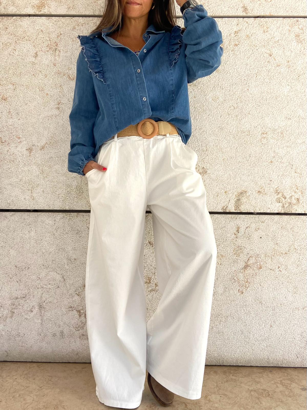 Modelo veste camisa azul de ganga com folhos e calças largas brancas com cinto bege.