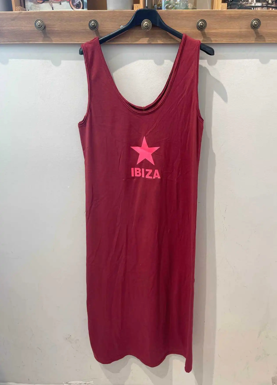 Vestido vermelho com estampado rosa 'IBIZA' e estrela pendurado em cabide preto numa parede branca