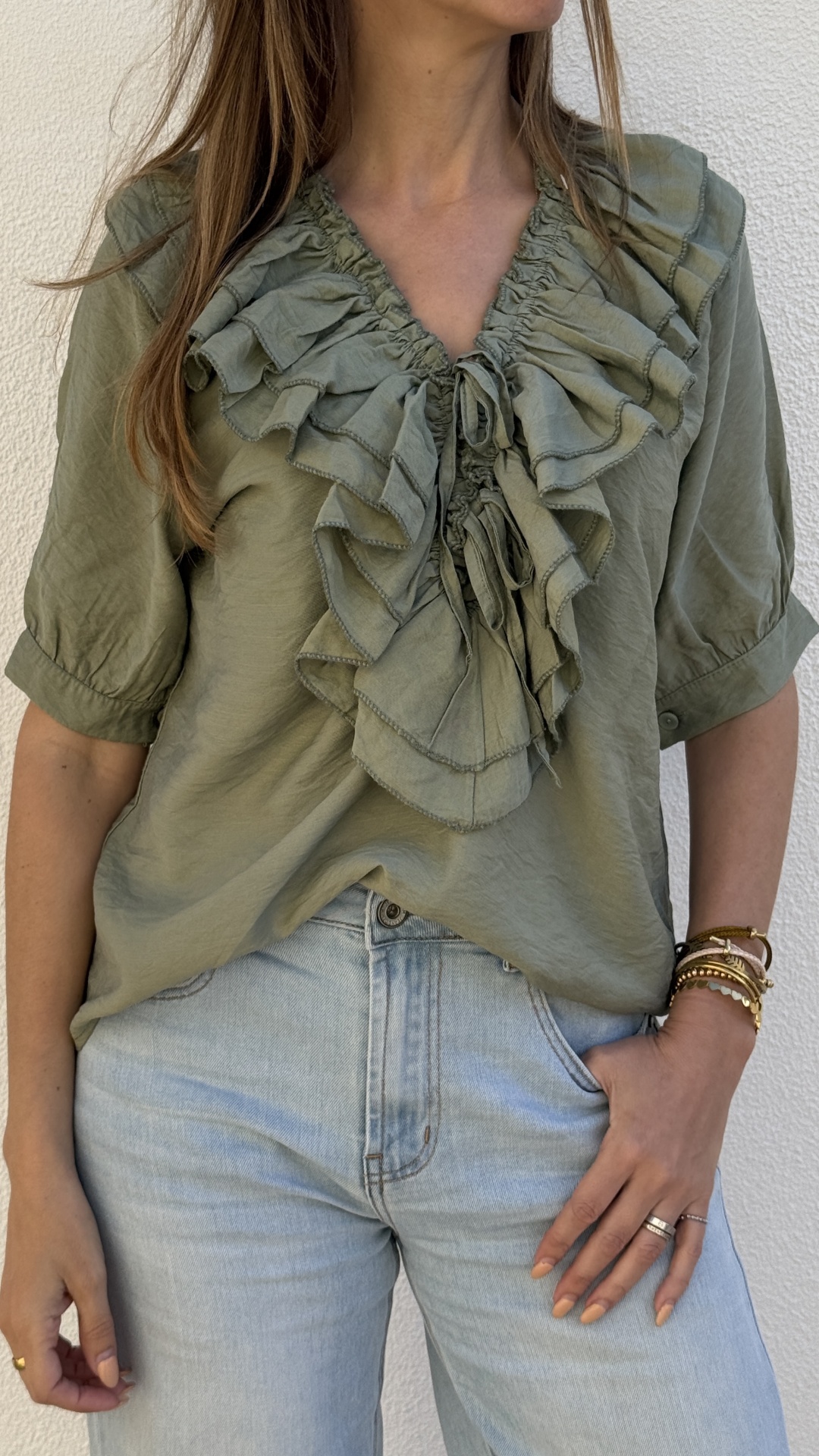 Blusa verde com folhos e laços no decote e jeans azul claro em fundo branco texturizado