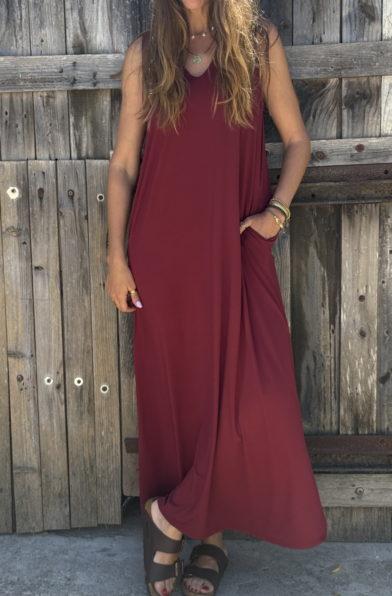 Vestido comprido bordô sem mangas com bolsos e sandálias castanhas em fundo de madeira
