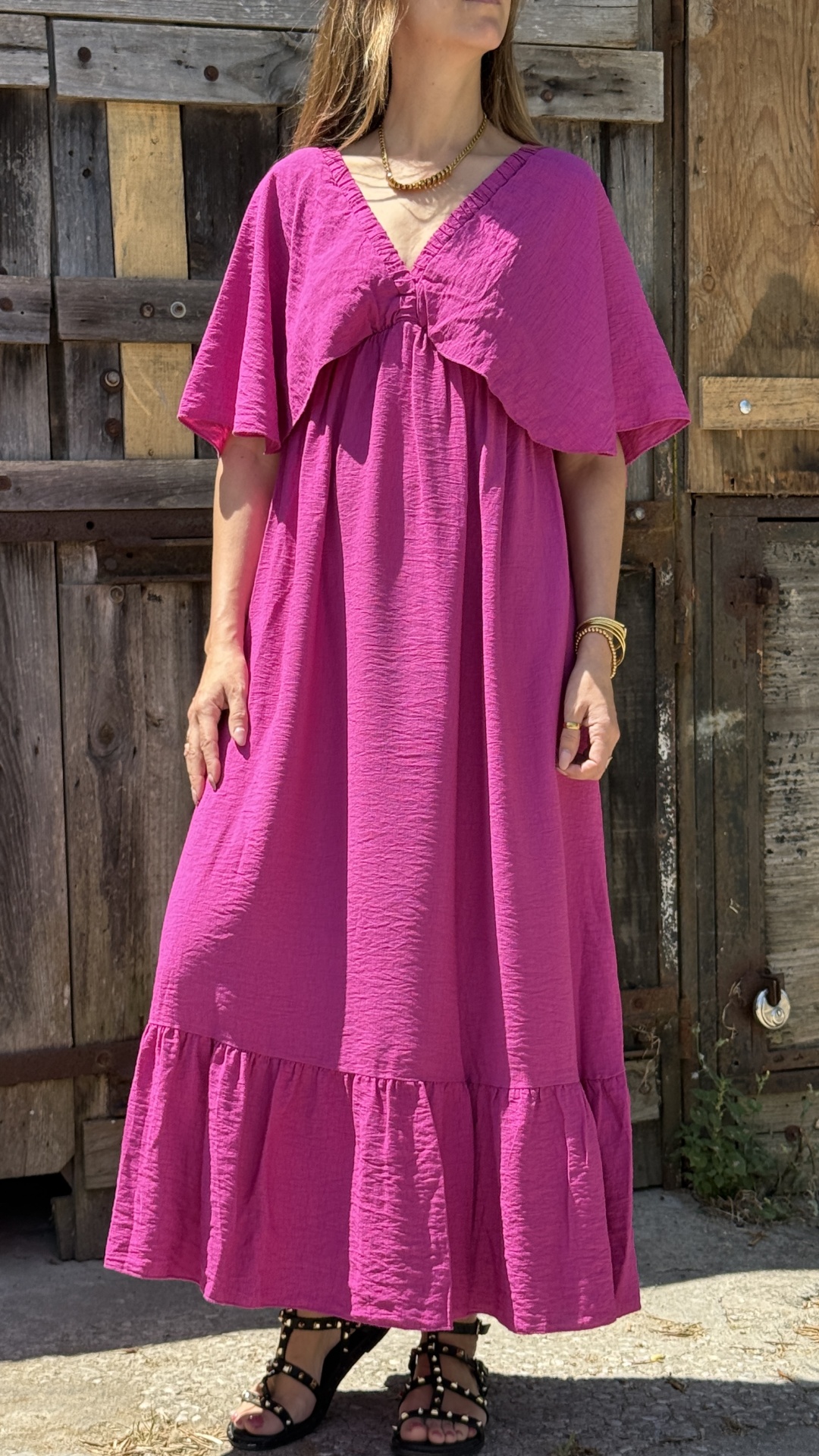 Vestido comprido rosa texturizado com decote em V e mangas largas, em fundo rústico exterior