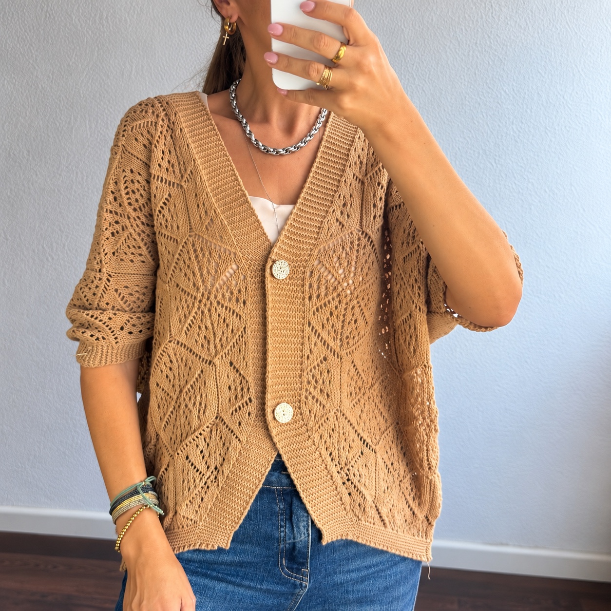 Cardigan castanho claro em malha aberta com padrão geométrico e botões, usado com jeans azul e acessórios