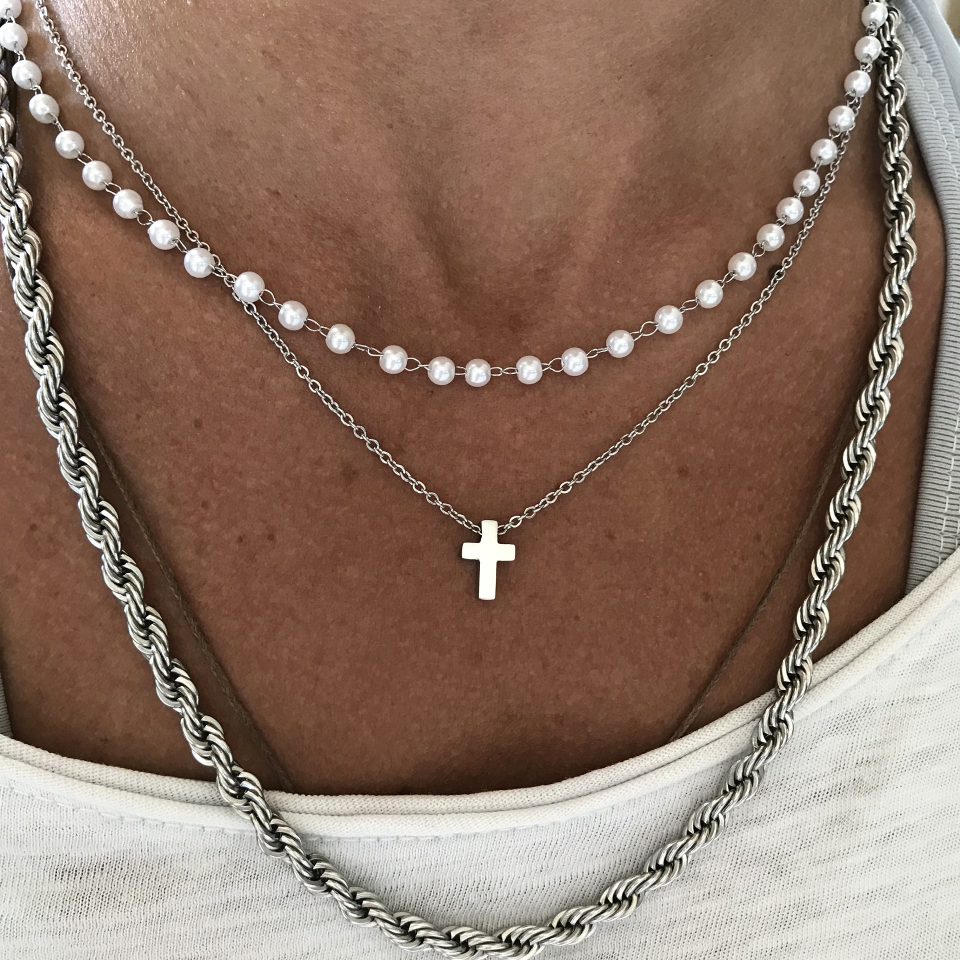 Colares de pérolas e prata com pendente de cruz sobre camisa branca