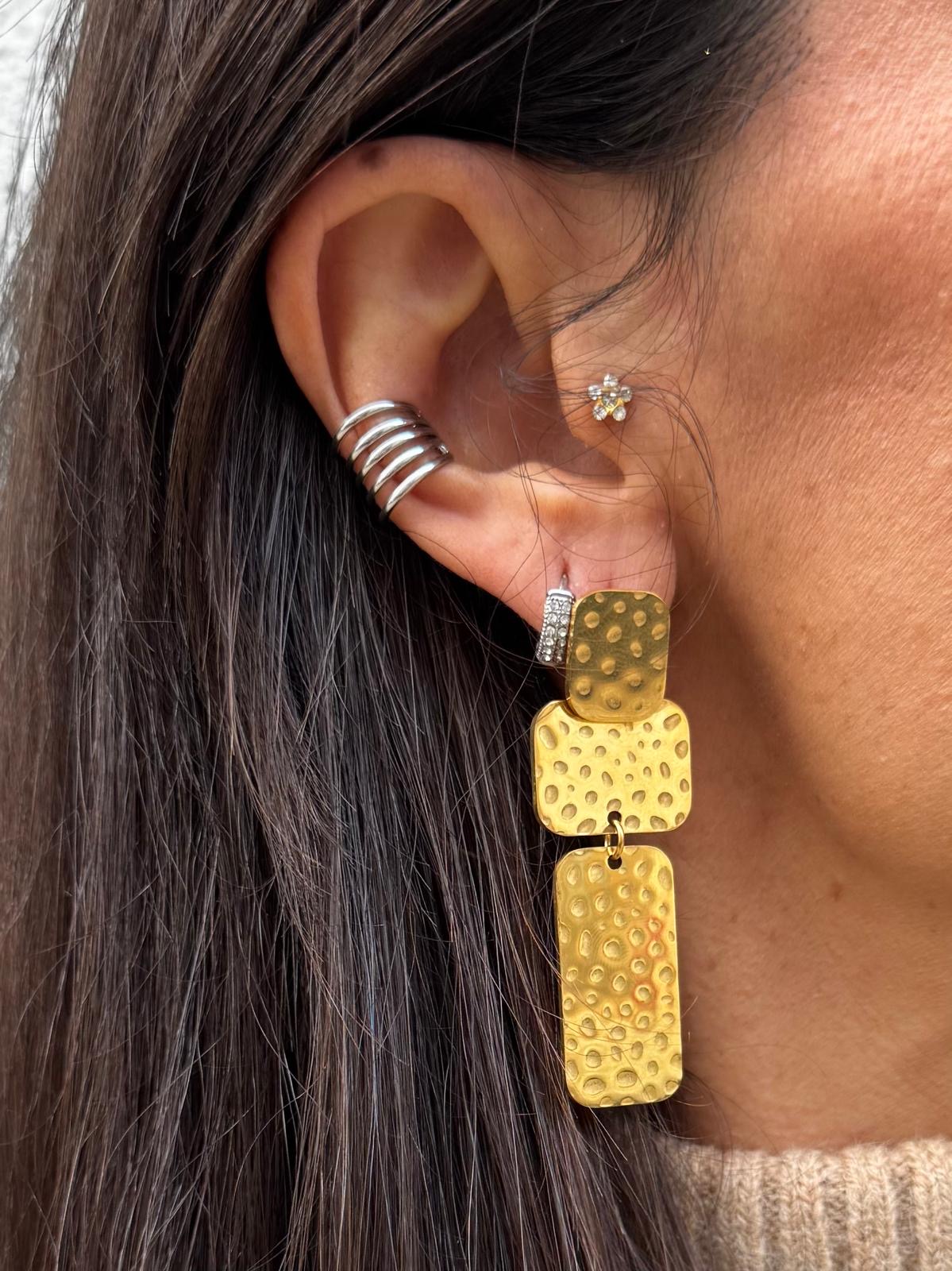 Brincos diversos numa orelha feminina, incluindo dourado martelado e prateado em espiral