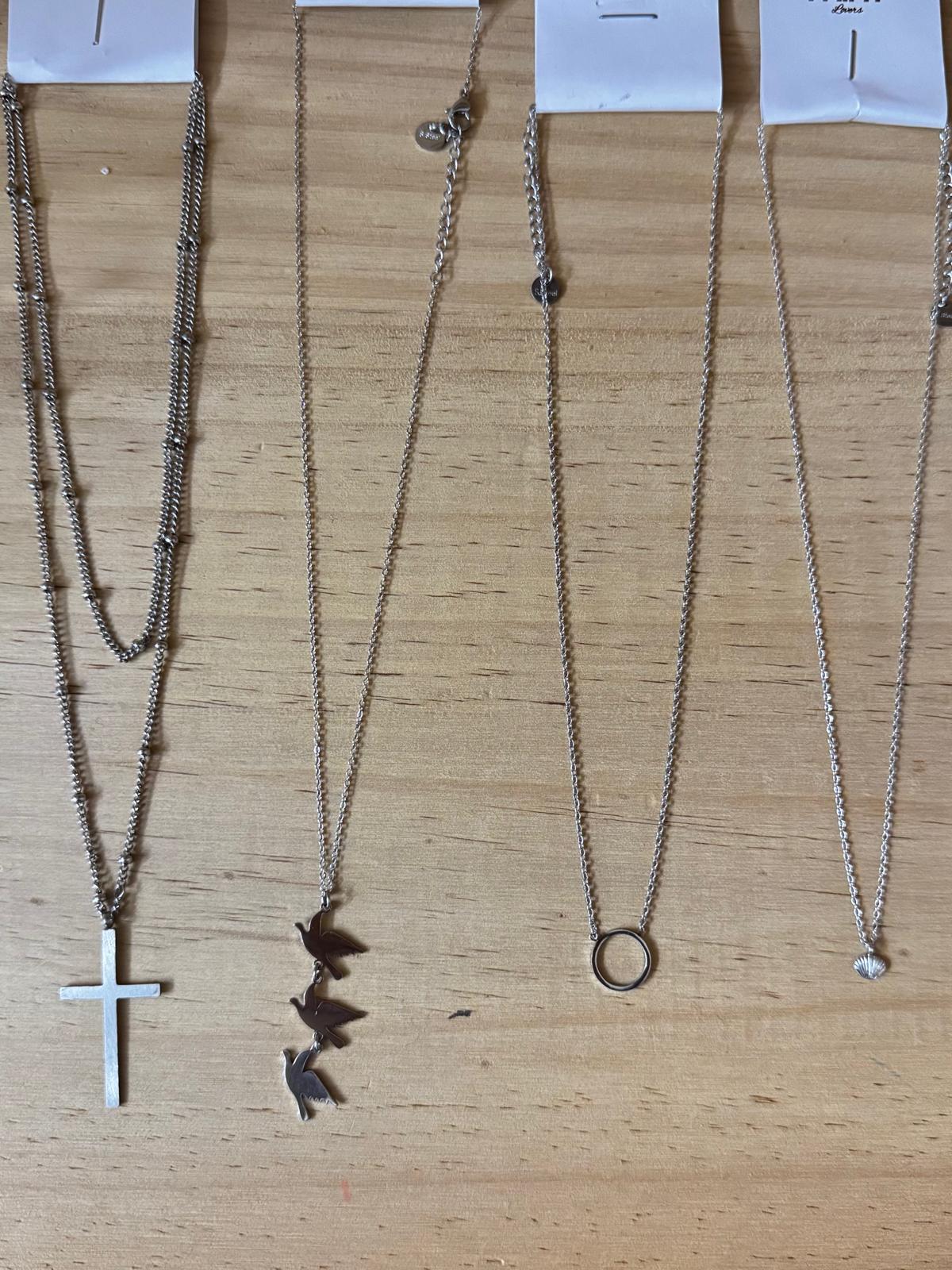 Quatro colares de prata com diferentes pendentes sobre madeira clara.