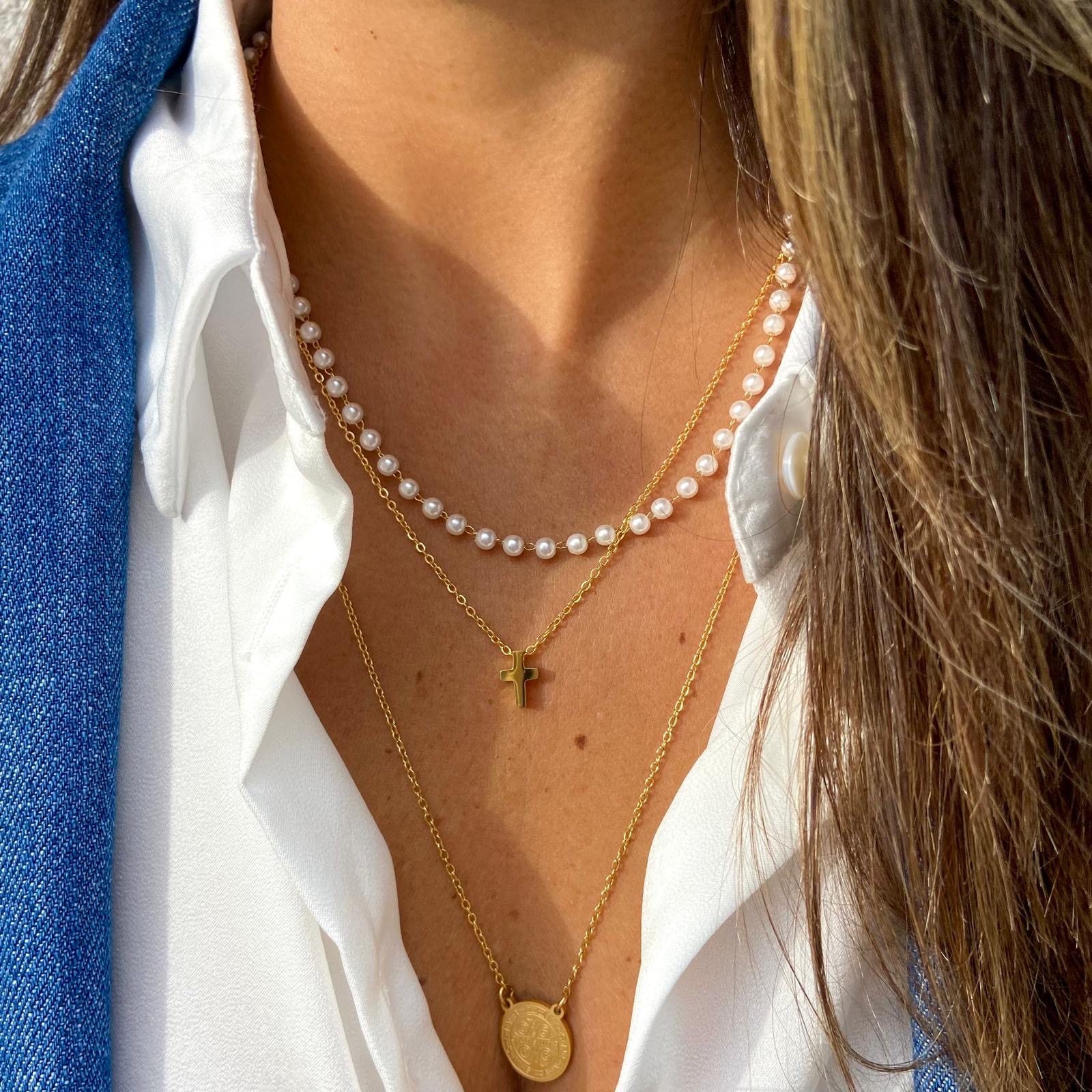 Colares duplos com pérolas e pendentes dourados em pessoa com camisa branca e casaco azul
