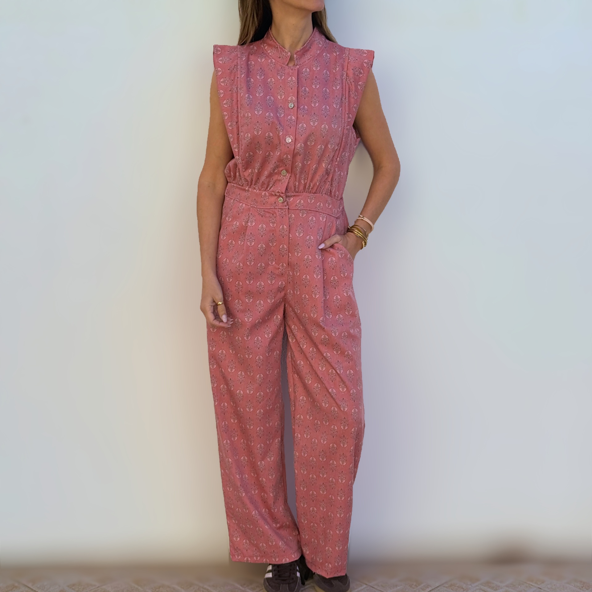 Macacão feminino rosa com padrão floral e botões na frente em fundo neutro.