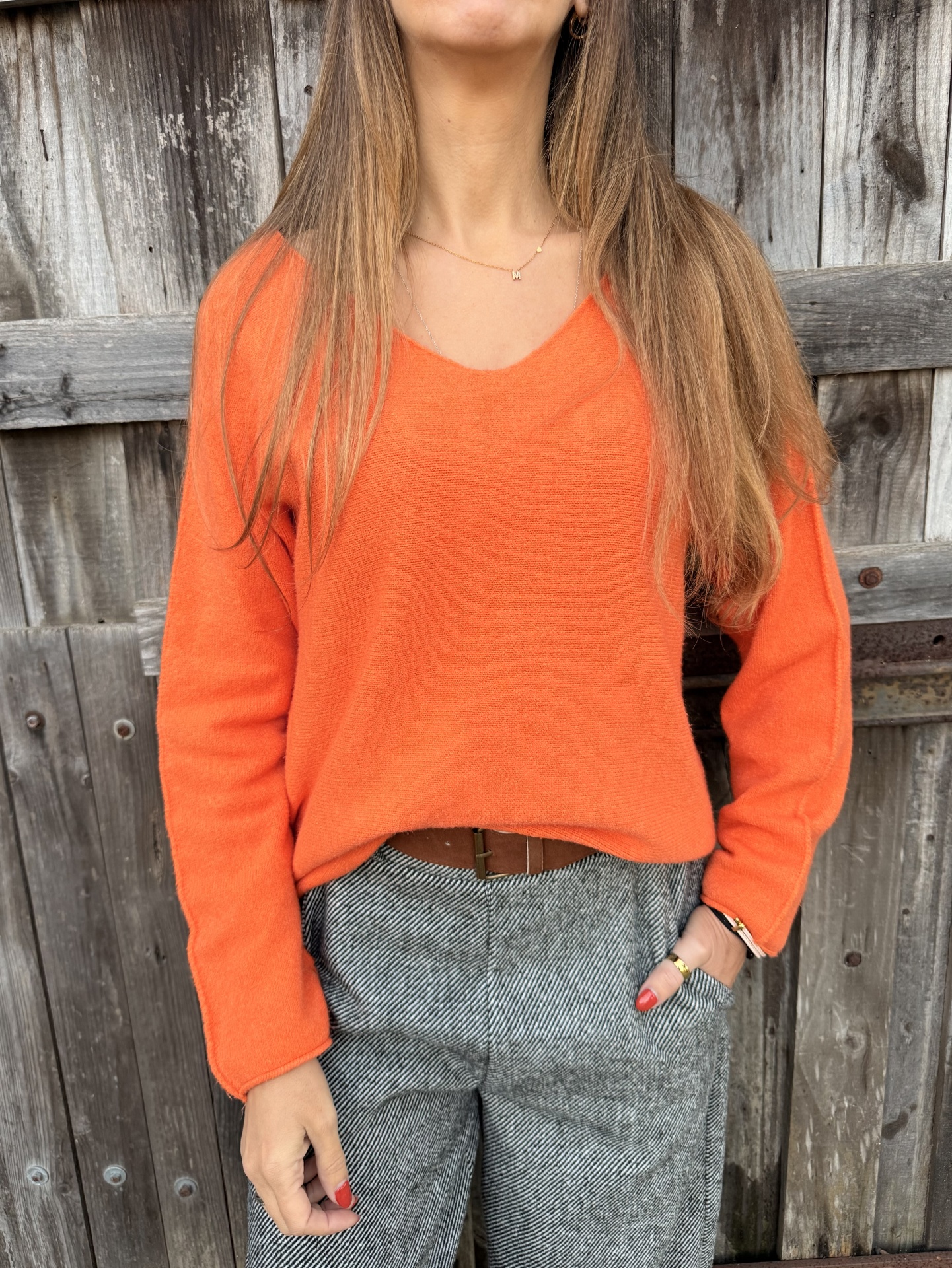 Camisola laranja com decote em V e calças cinzentas padrão espinha de peixe