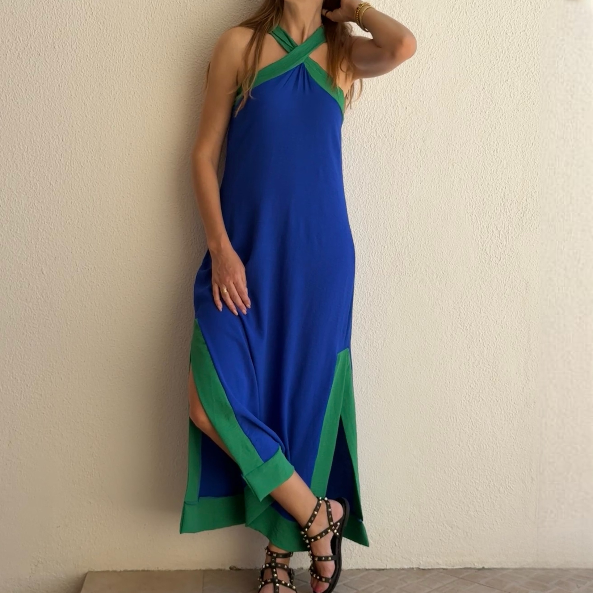 Vestido azul com detalhes verdes e sandálias pretas em mulher junto a parede branca.