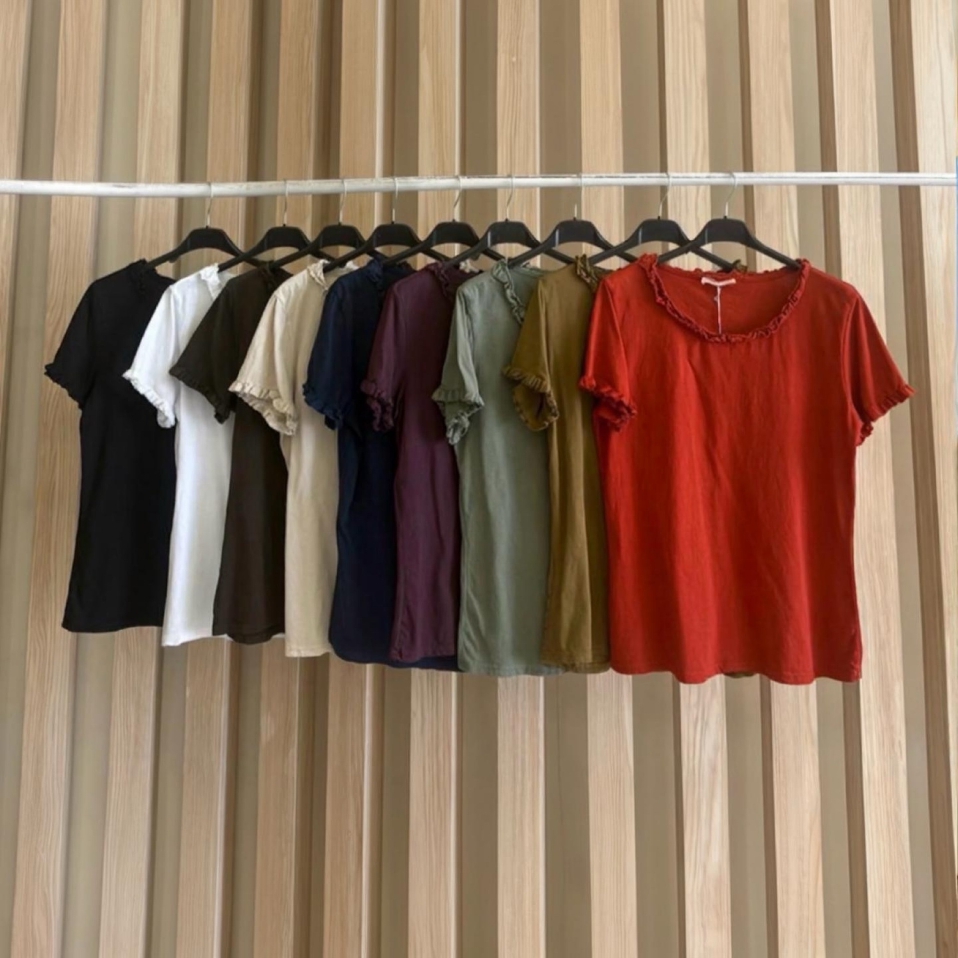 Blusas de manga curta em vários tons penduradas em cabides pretos num suporte branco