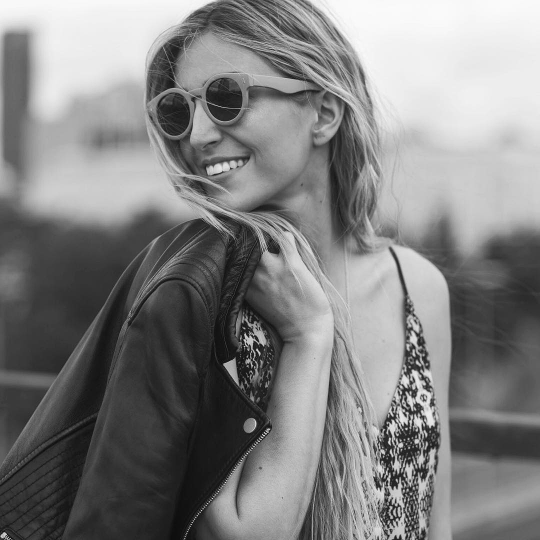 Mulher com óculos de sol redondos, top padrão preto e branco e jaqueta de couro preta ao ombro