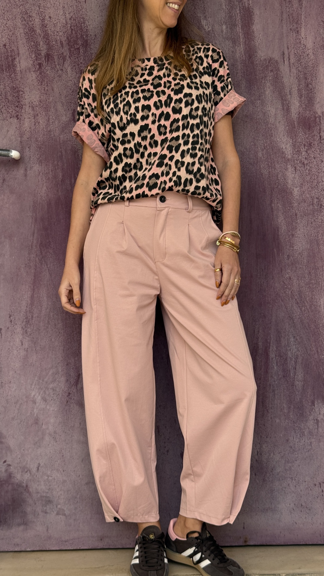 Mulher com t-shirt animal print e calças rosa largas junto a parede roxa