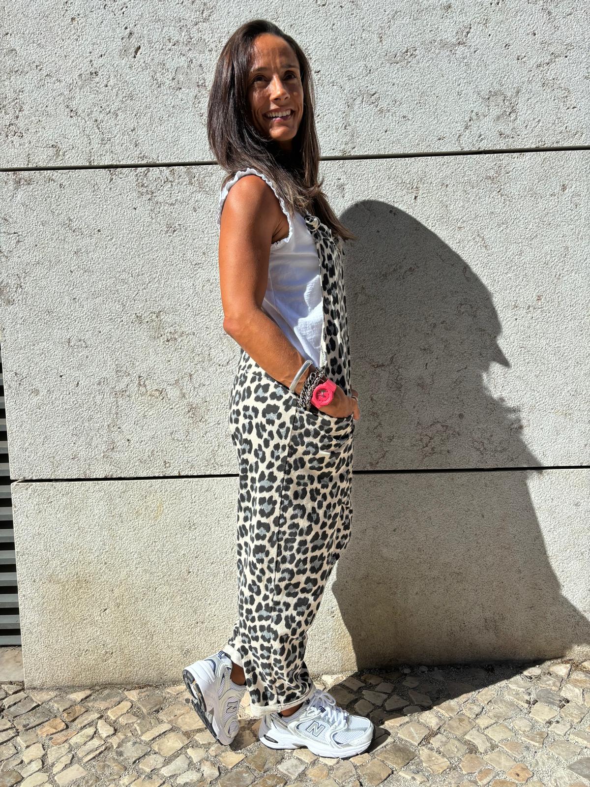 Mulher com calças de padrão leopardo, camisola branca e ténis brancos ao ar livre junto a parede de pedra cinzenta