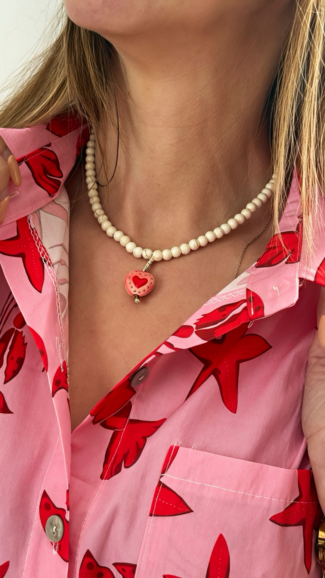 Colar de contas creme com pendente em forma de coração vermelho e rosa no pescoço