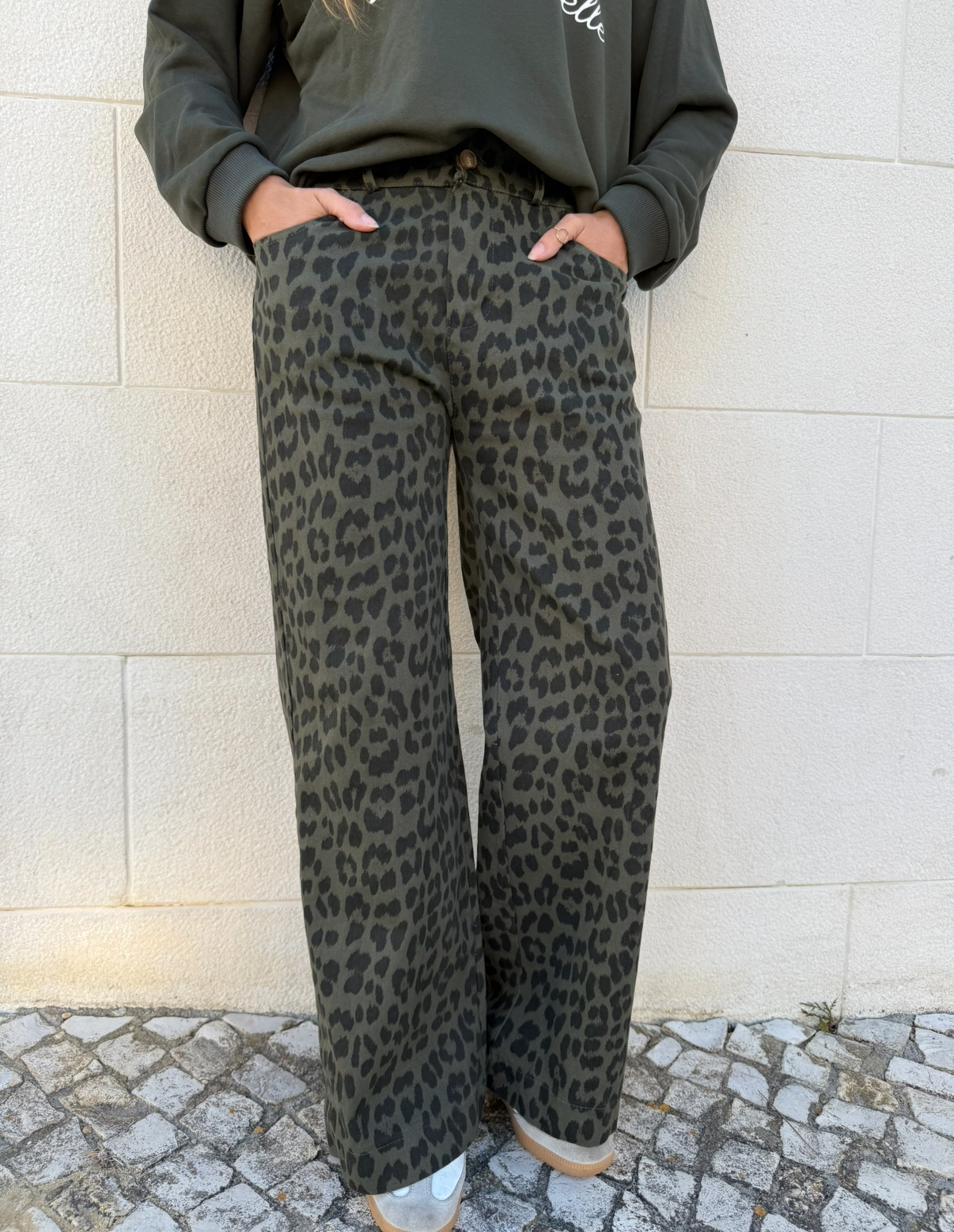 Calças com padrão animal print em tons de verde e preto junto a parede clara.