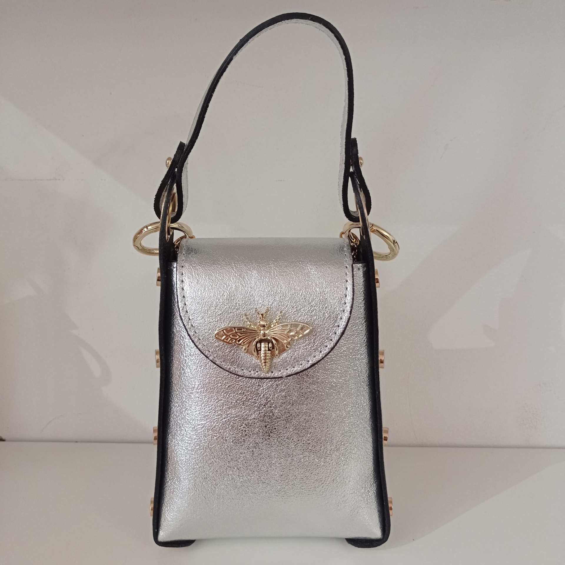 Mala pequena prateada com alça preta e fecho dourado em forma de abelha