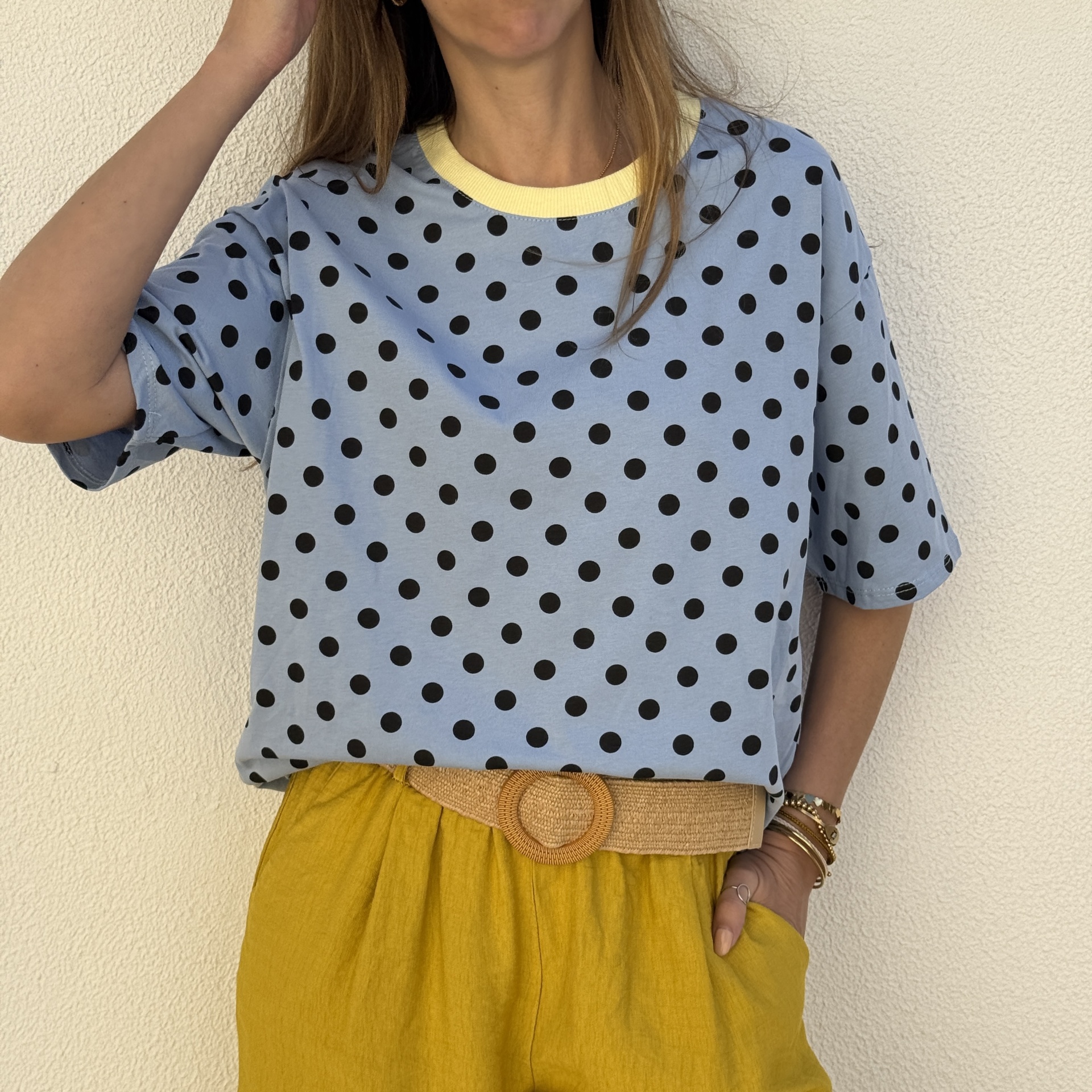 T-shirt azul claro com bolinhas pretas e gola amarela, calças amarelas e cinto de tecido natural