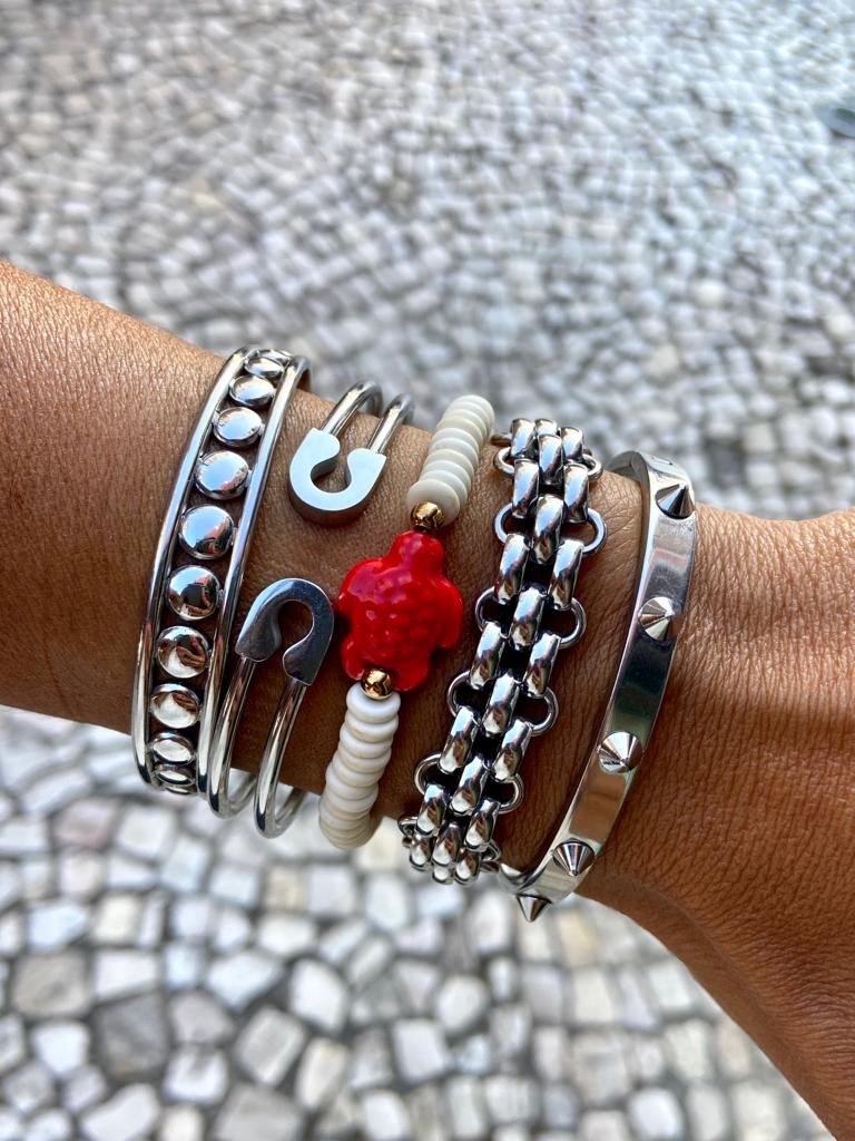 Várias pulseiras metálicas e de contas brancas e vermelhas no pulso, fundo de calçada