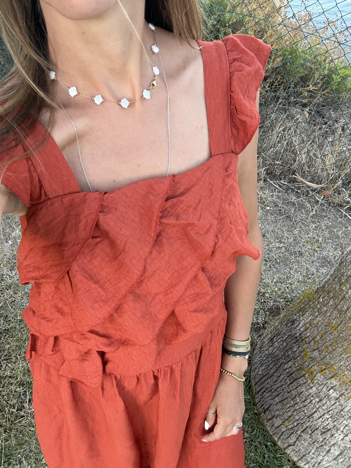 Vestido laranja com folhos, colar dourado com pendentes brancos e pulseiras, em ambiente exterior
