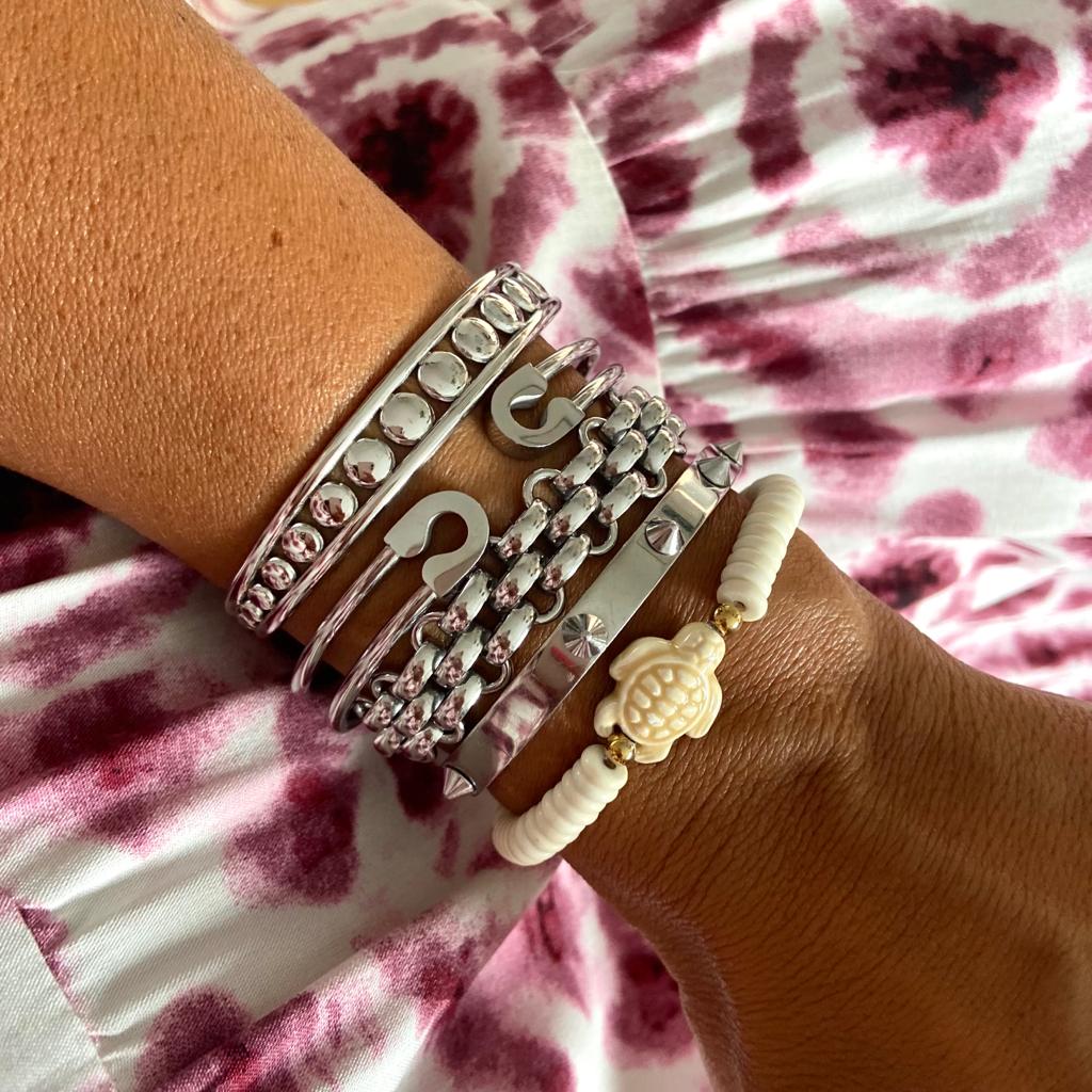 Vários braceletes prateados e um branco com tartaruga no pulso sobre tecido rosa e branco