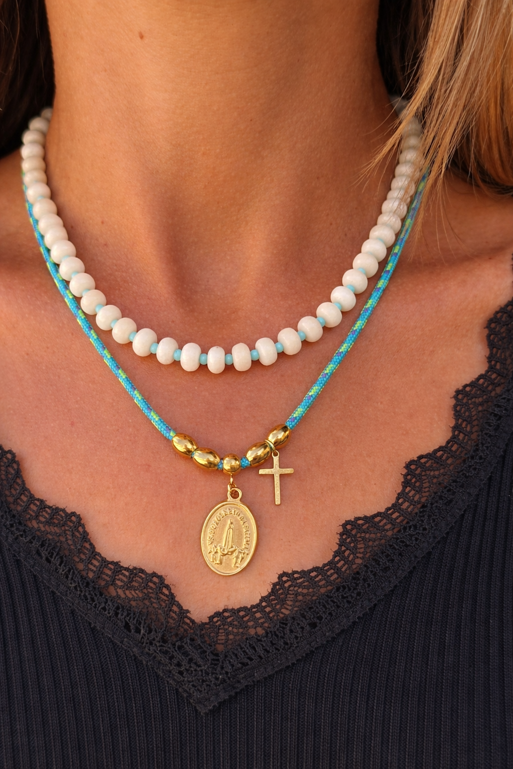 Colar branco e azul com medalha e cruz dourada no pescoço