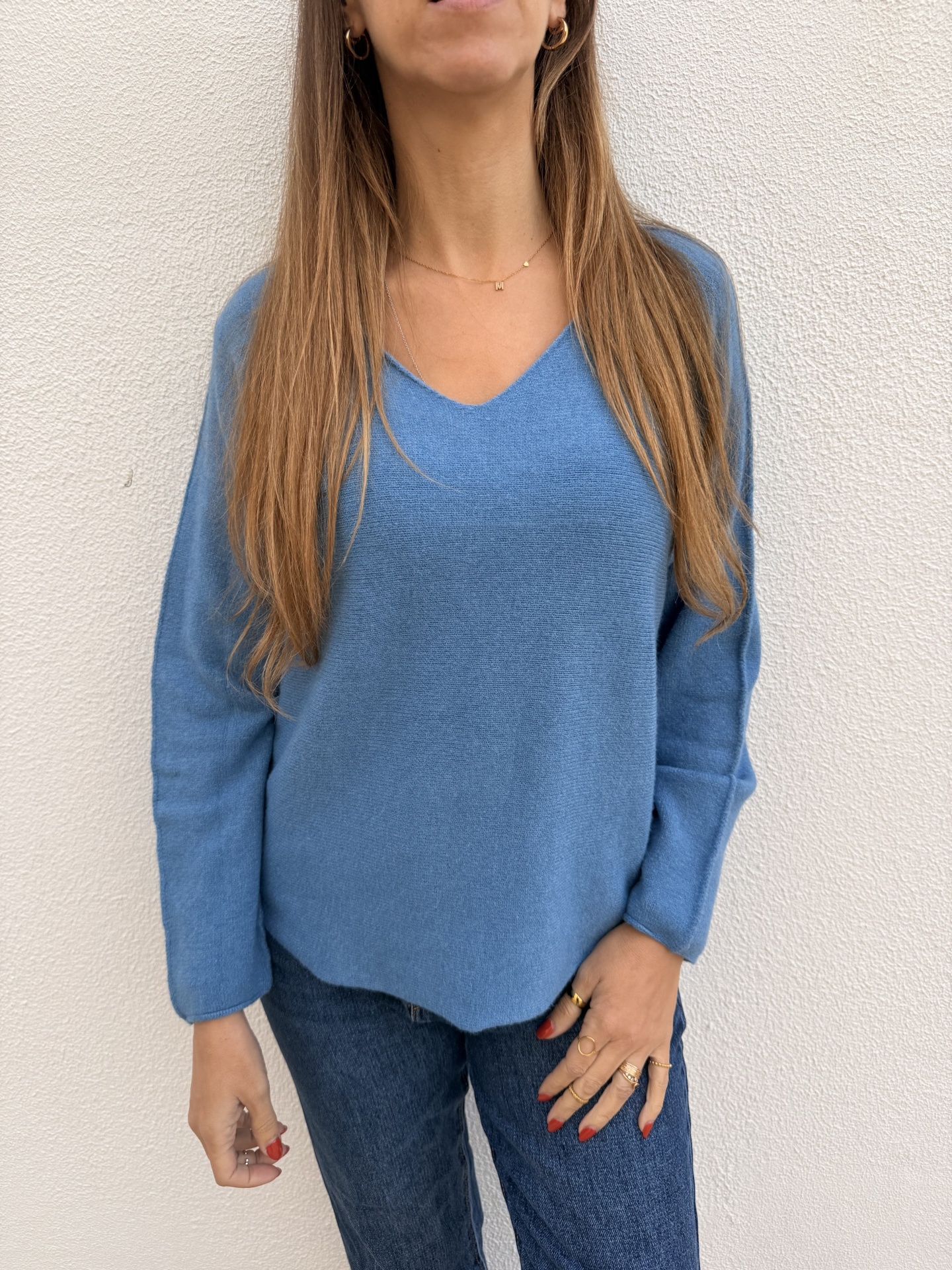 Mulher com camisola azul de malha e calça de ganga diante de parede branca