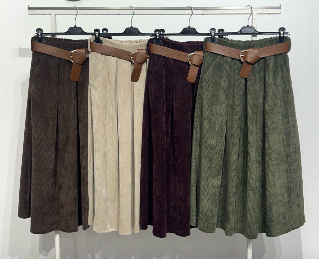 Quatro saias plissadas de veludo cotelê com cintos castanhos em diferentes cores penduradas numa barra metálica.