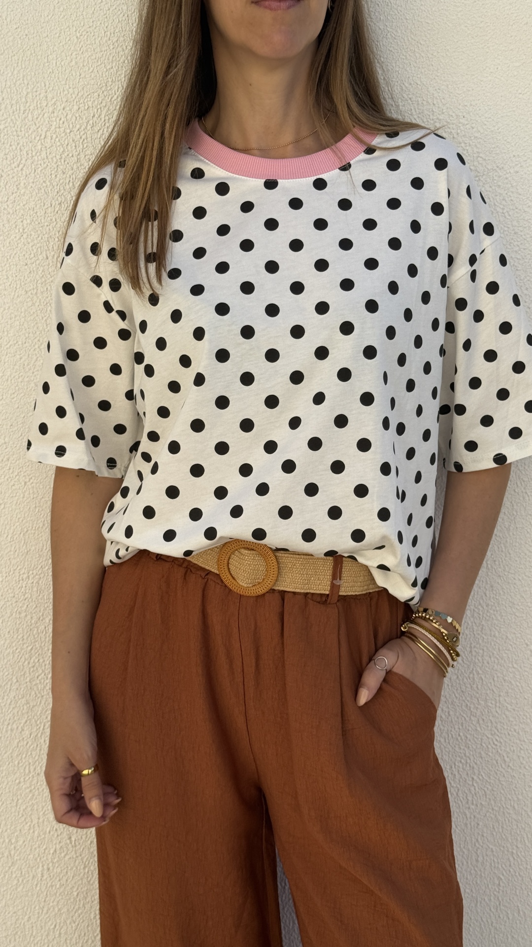 T-shirt feminina branca com bolinhas pretas e gola rosa com calças castanhas e cinto de palha