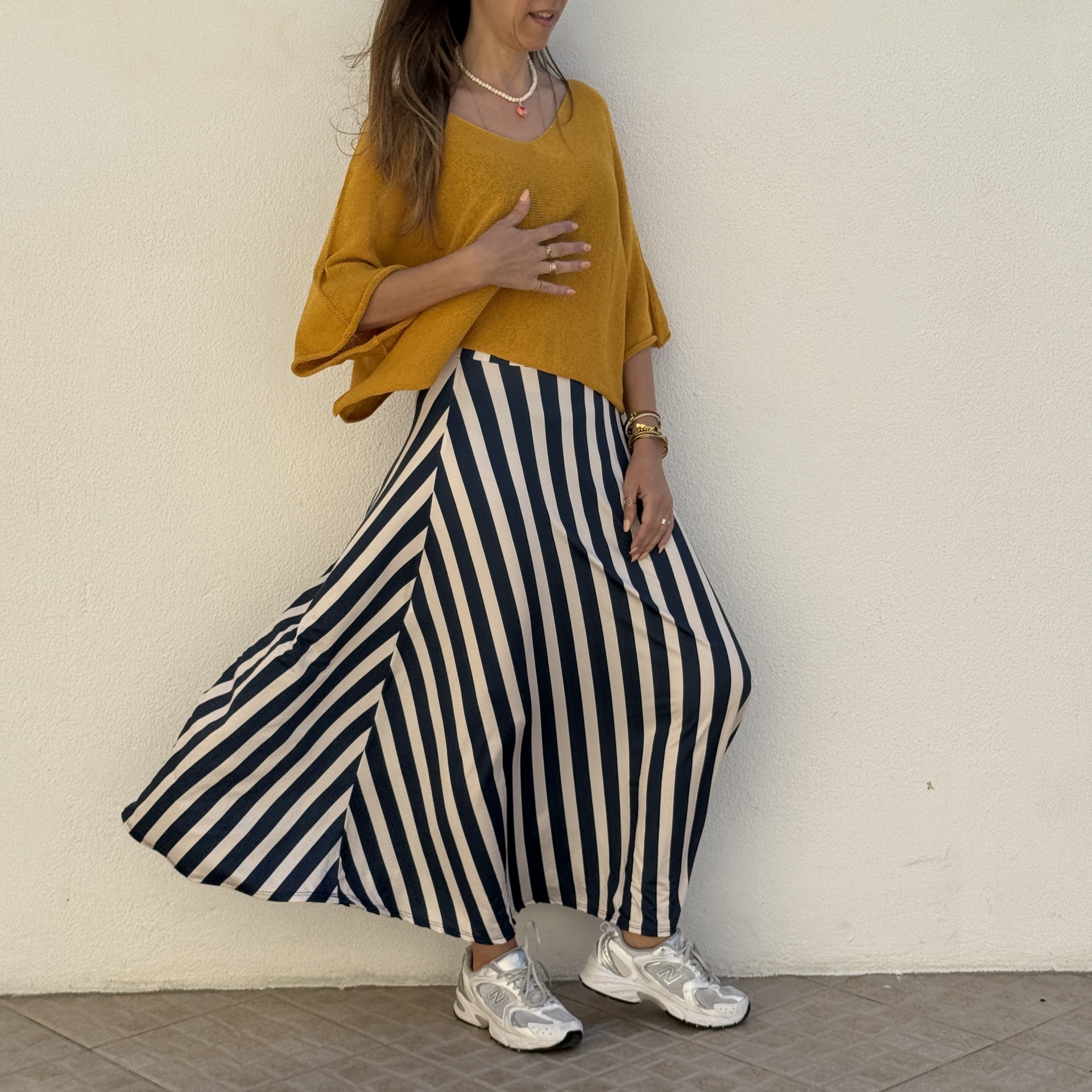 Mulher com sweater amarelo e saia listrada azul e branca com sapatilhas brancas