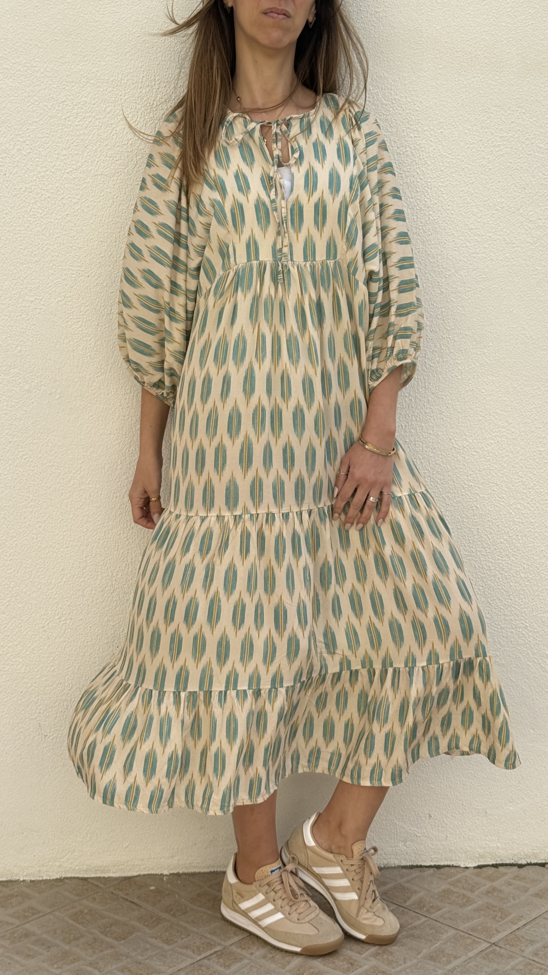 Vestido comprido com padrão azul e bege e ténis bege com riscas brancas.