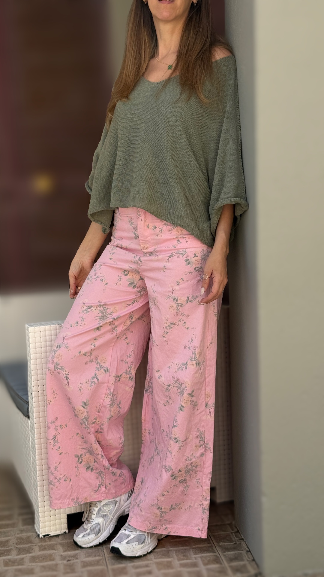 Mulher com calças largas rosa com flores, blusa verde larga e sapatilhas brancas