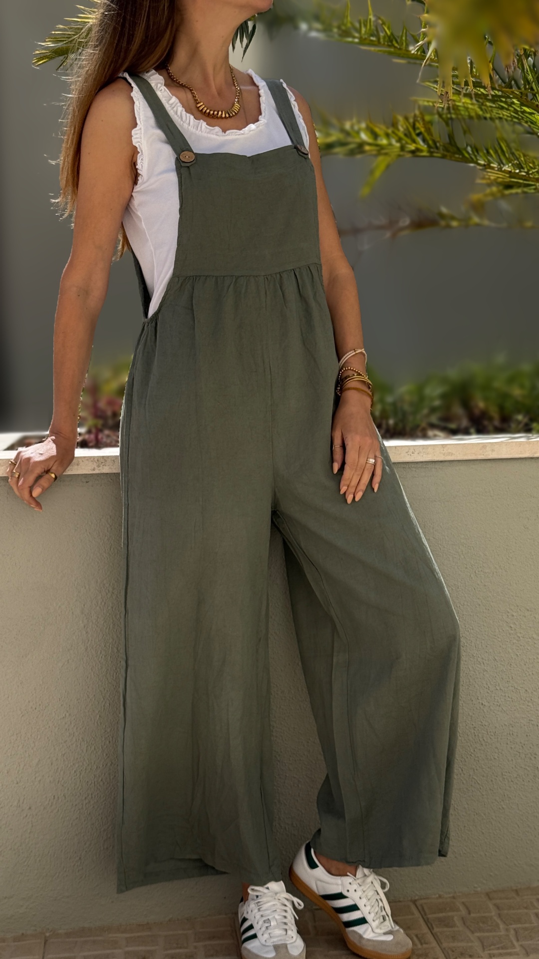 Macacão verde de tecido leve com alças e botões usado sobre t-shirt branca e ténis brancos com riscas verdes