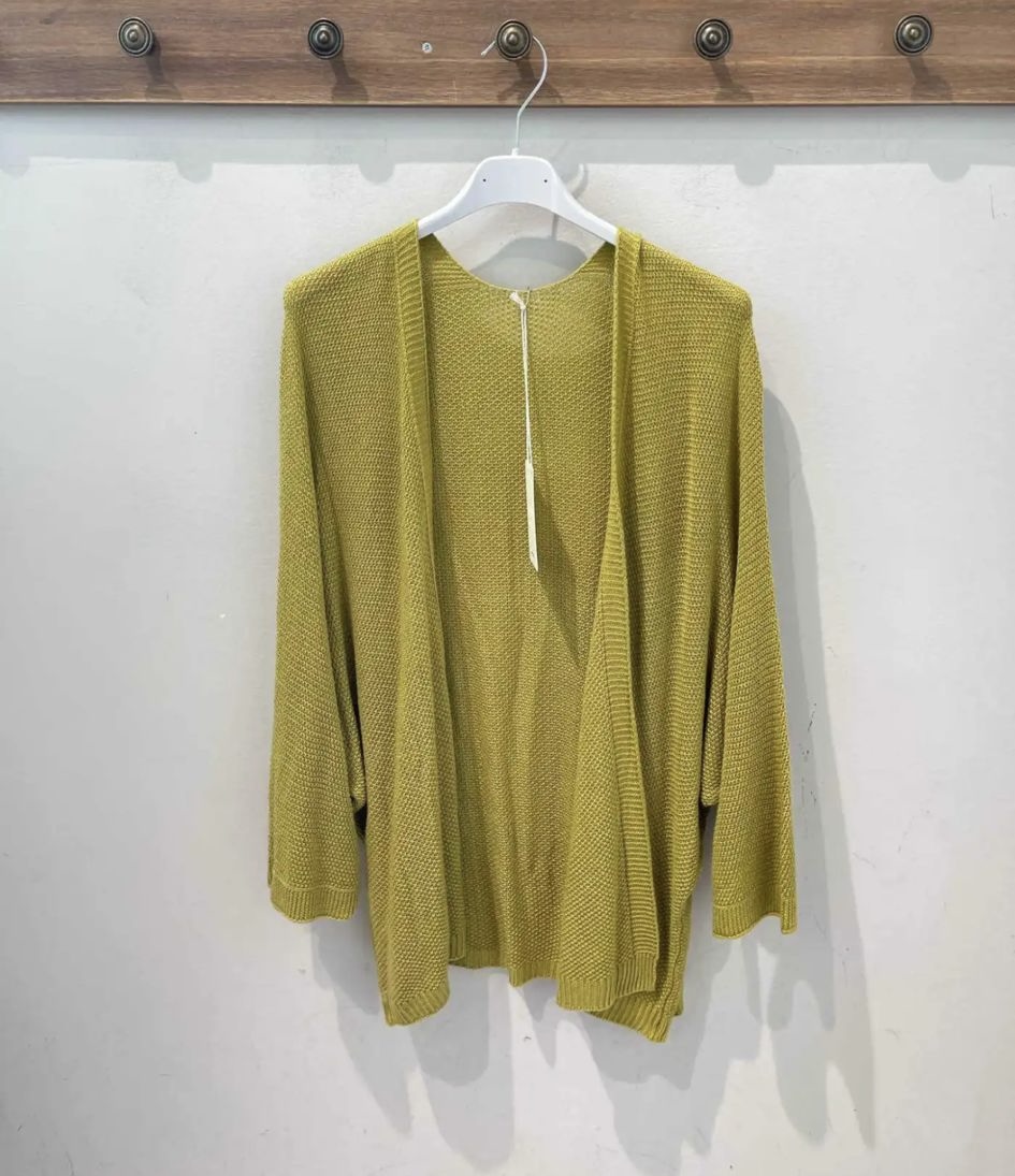 Casaco aberto de malha verde-oliva pendurado num cabide branco junto a cabideiro de madeira.