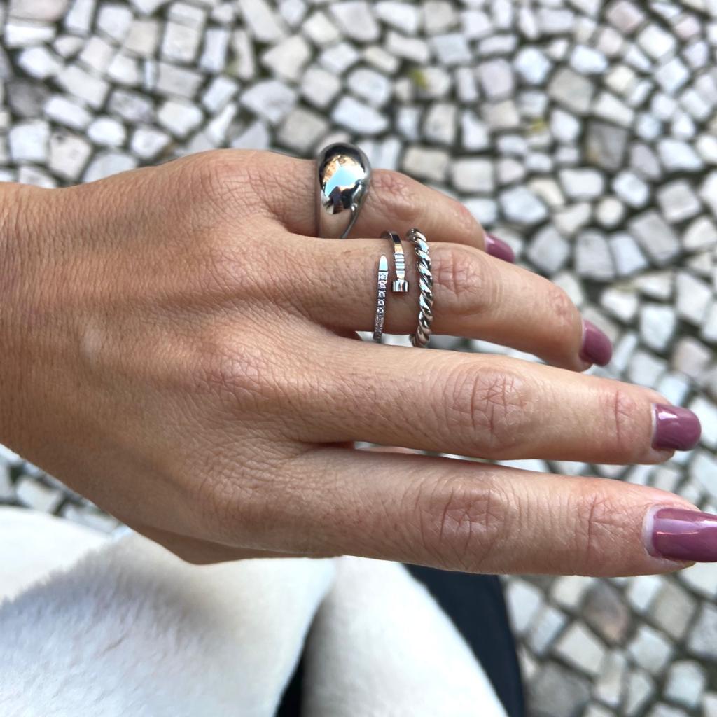 Mão feminina com três anéis prateados e unhas rosa escuro sobre calçada de pedra