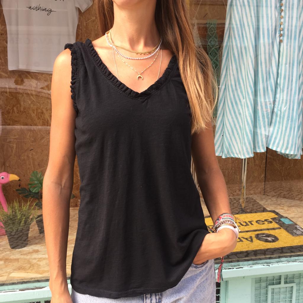 Regata preta com decote em V e detalhe franzido em mulher à frente de loja.