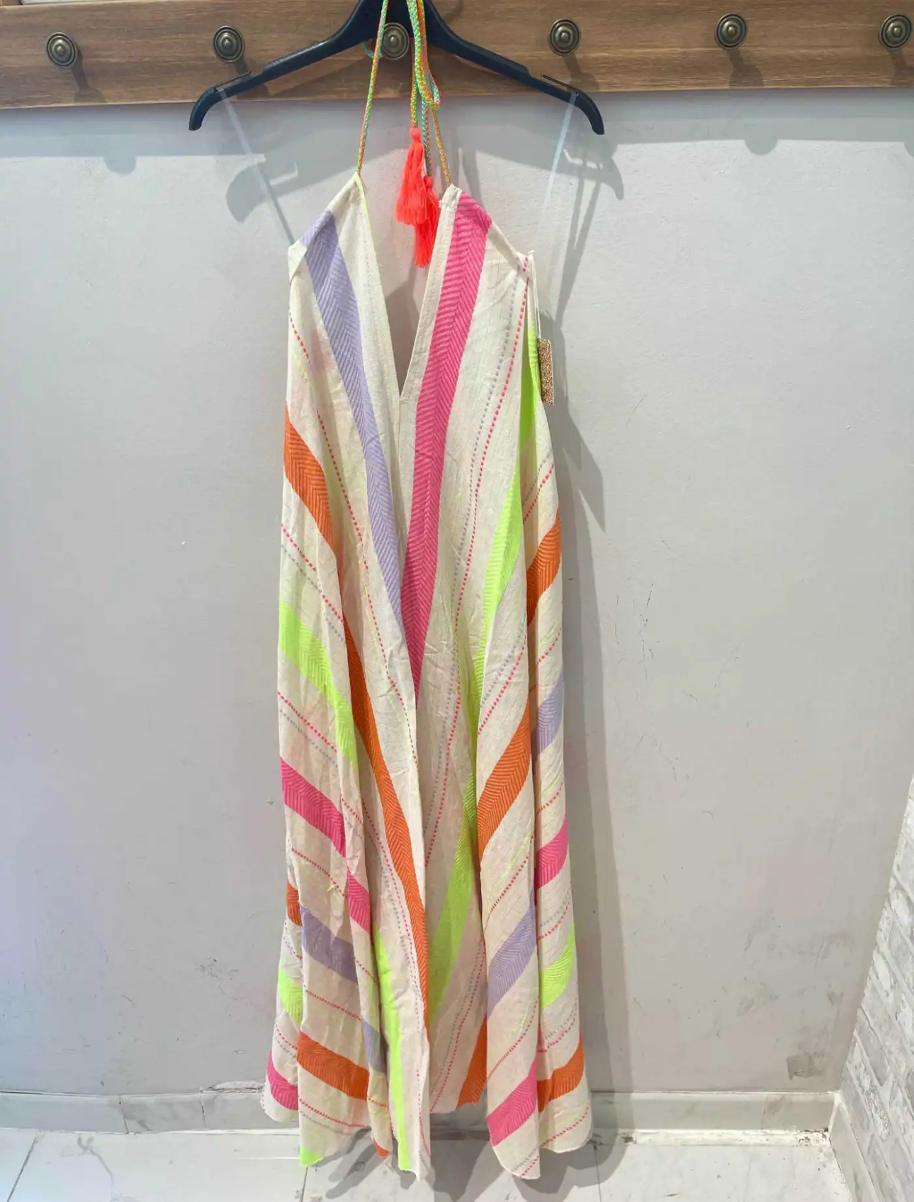 Vestido leve com riscas coloridas pendurado num cabide preto na parede