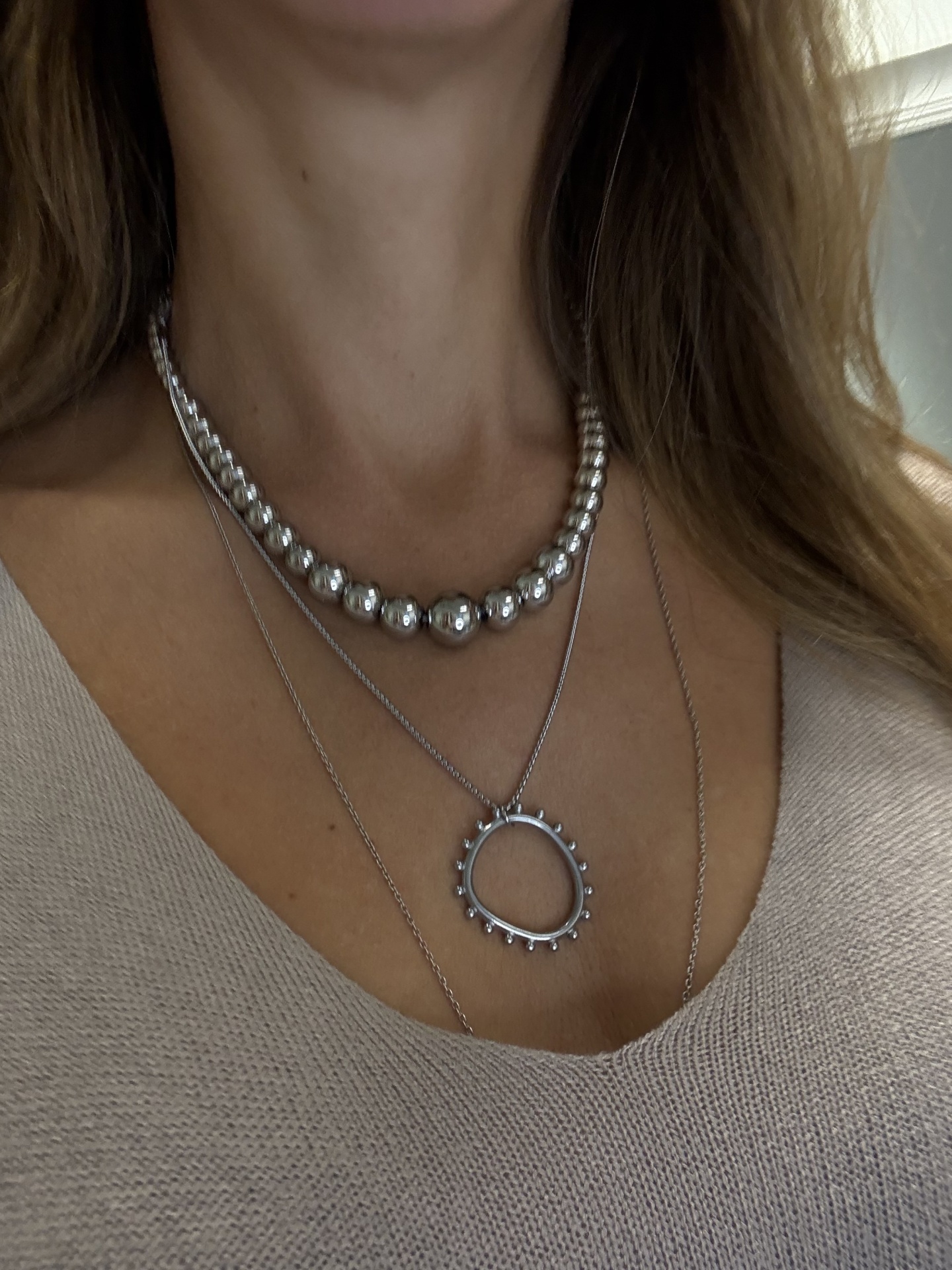 Colares prateados com bolas e pendente circular sobre blusa bege de malha