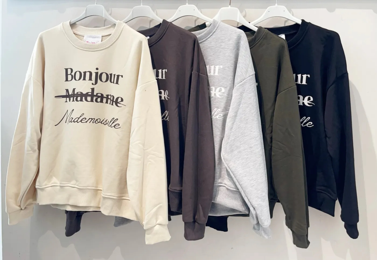 Sweatshirts de várias cores com texto Bonjour Madame Mademoiselle penduradas em cabides