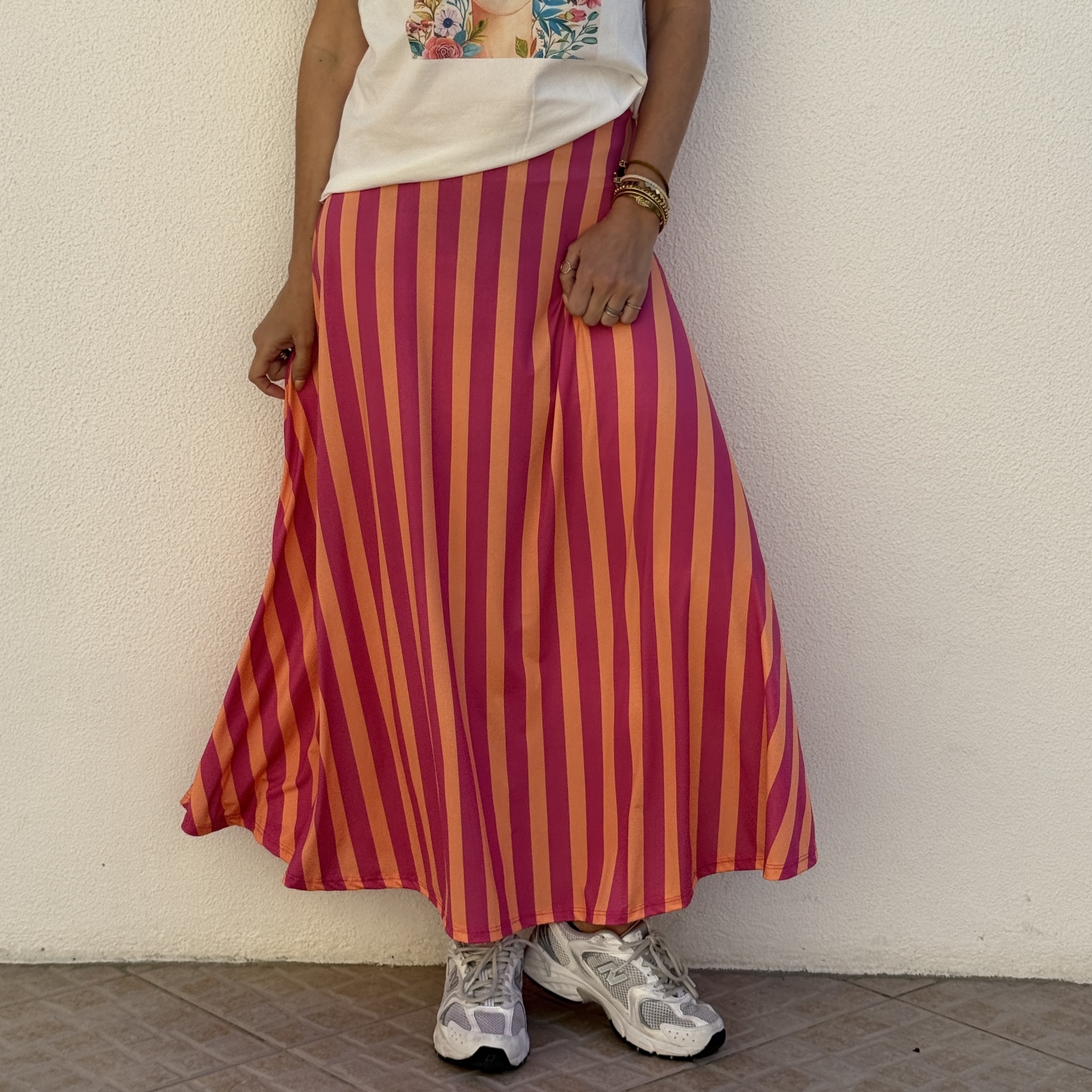 Saia comprida de riscas laranja e rosa, ténis brancos e t-shirt branca com estampado floral.