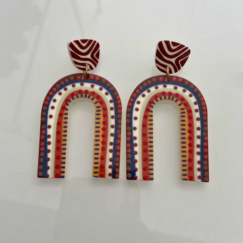 Brincos coloridos em forma de arco com padrão de linhas onduladas em vermelho e branco na base