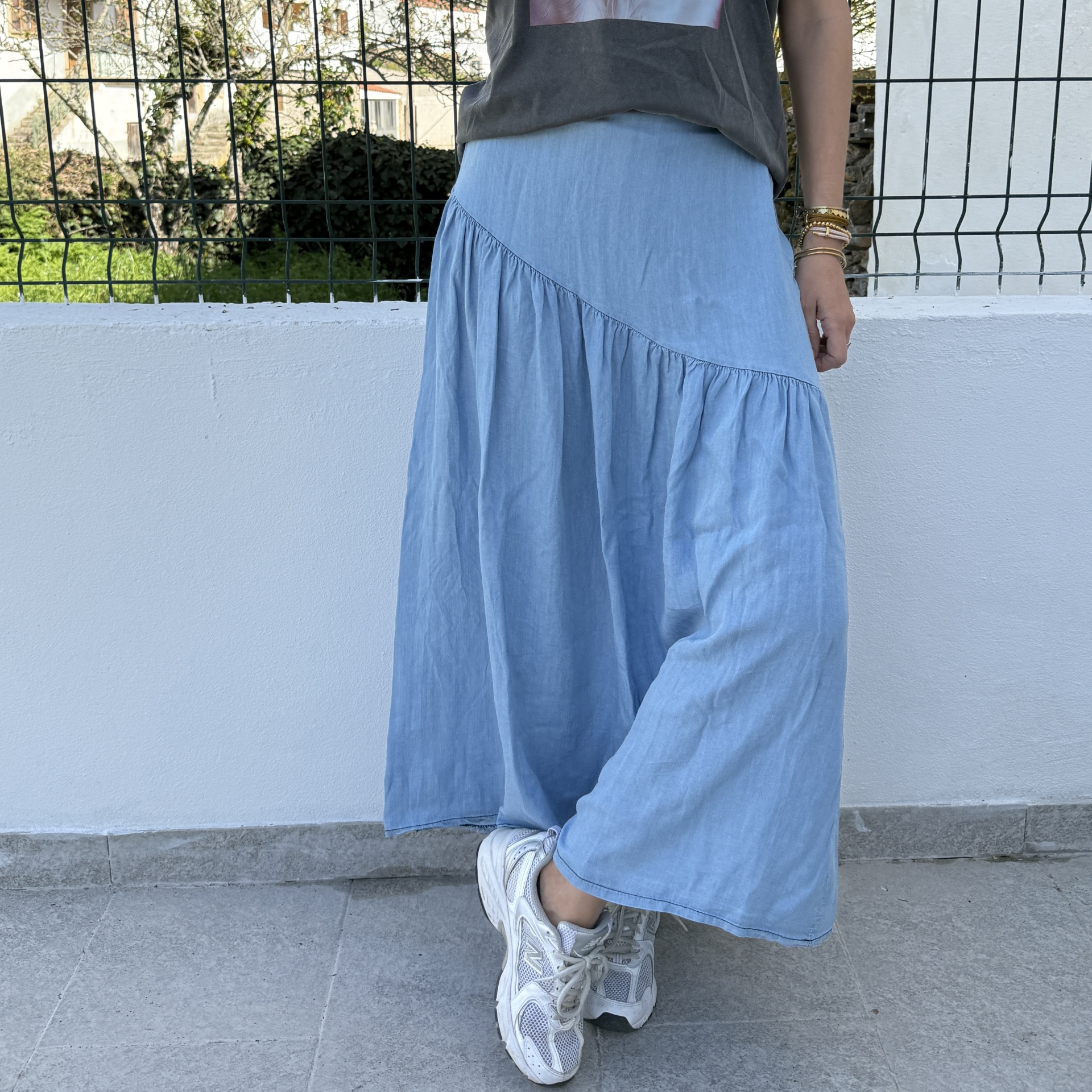 Saia azul clara assimétrica com pregas, t-shirt cinza escuro e ténis brancos