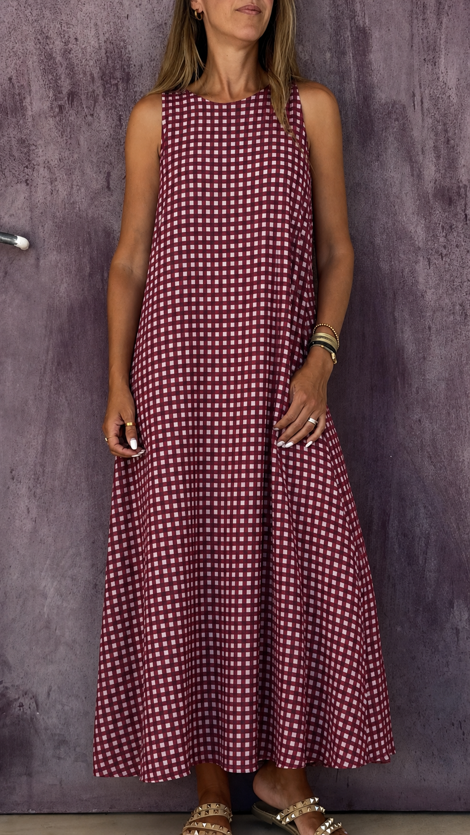 Vestido comprido vermelho com padrão quadriculado branco em mulher, sandálias bege com tachas.