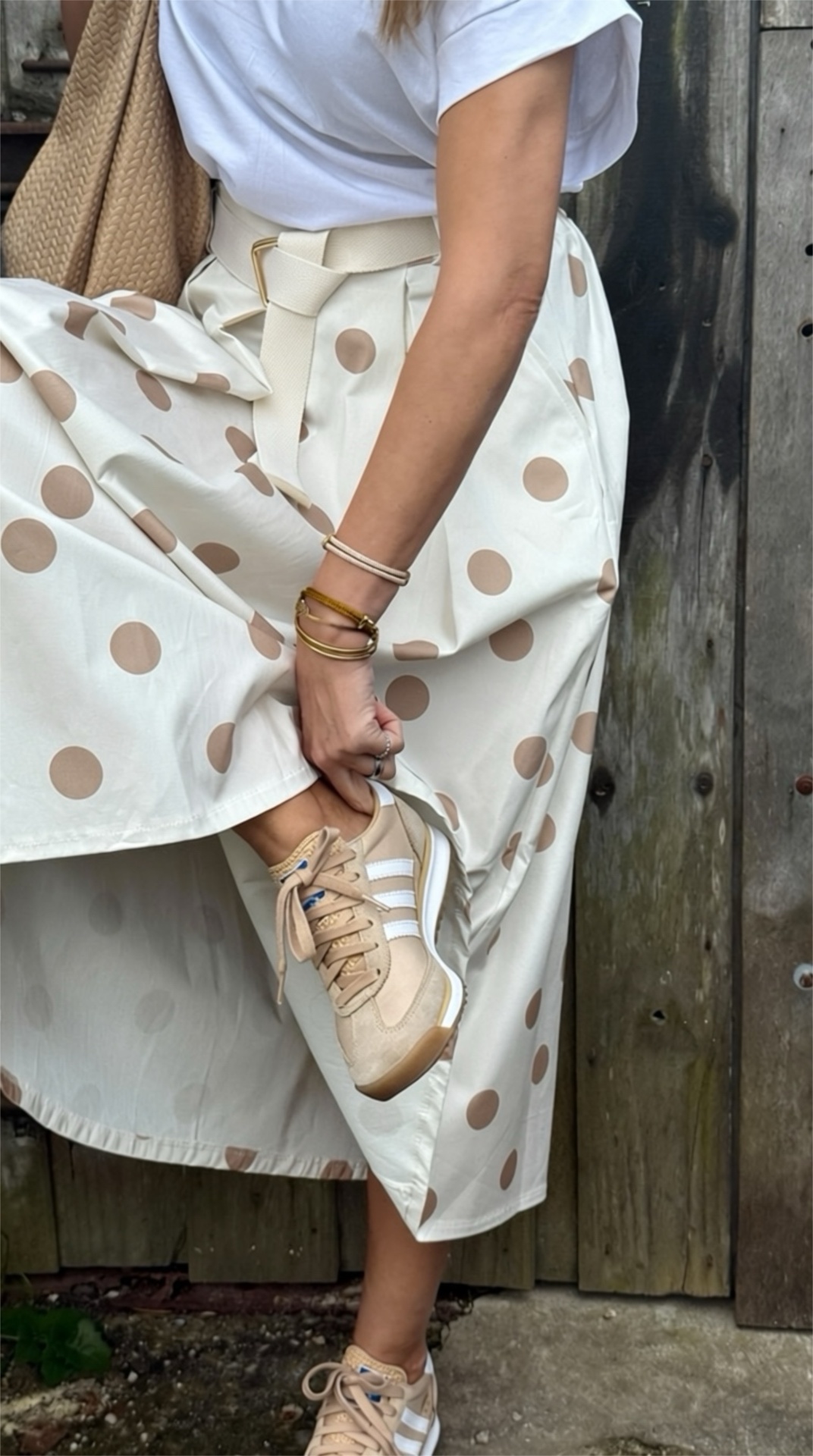 Saia creme com bolinhas castanhas, cintinho creme, t-shirt branca, sapatilhas bege com riscas brancas, fundo madeira