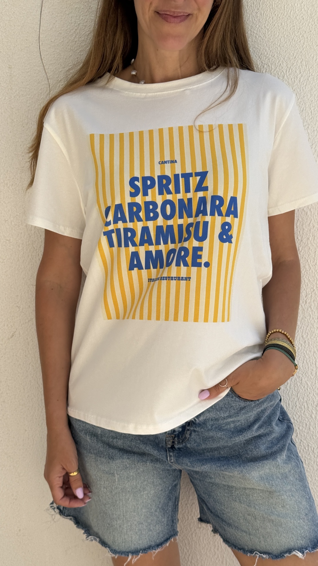 T-shirt branca com estampado amarelo e texto azul, calções jeans azuis desfiados